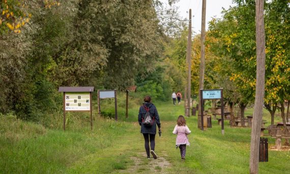 A parent and child walking on a path in a scenic nature reserve in Croatia, surrounded by lush greenery.